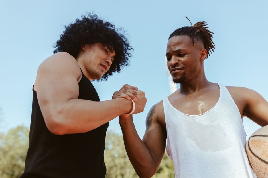 Two male basketball players engaging in a friendly handshake outdoors on a sunny day.