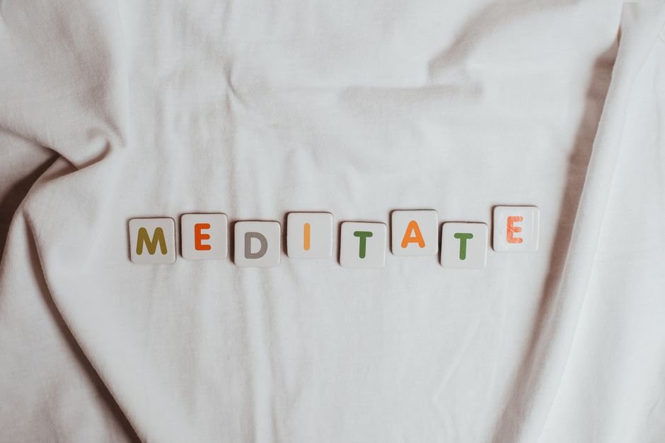 Colorful letter tiles spell 'meditate' on soft white fabric. Perfect for mindfulness themes.