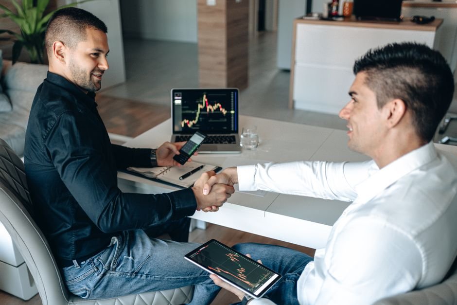 Two businessmen shake hands over a successful stock trading agreement using technology in a modern office.