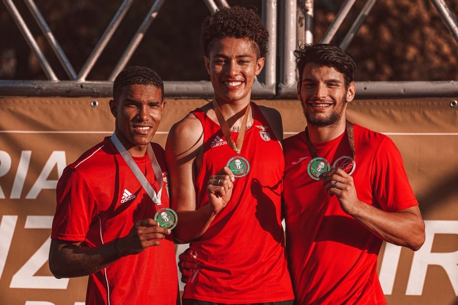Three athletes posing with medals, smiling after a victory outdoors. Embracing team spirit.
